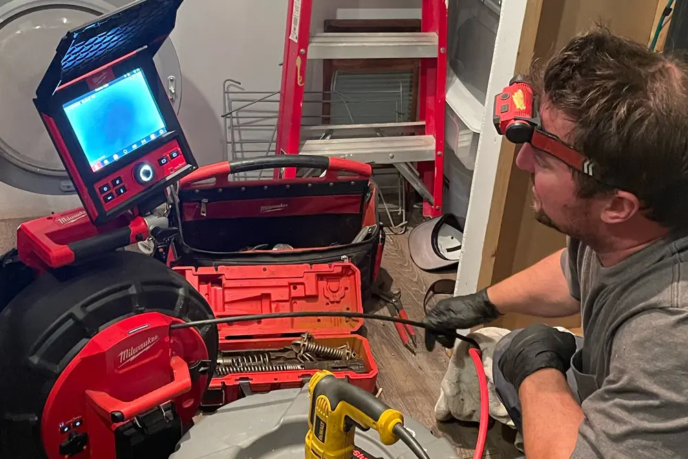 Calgary plumber performing sewer camera inspection with Milwaukee inspection equipment to diagnose residential drain problems.