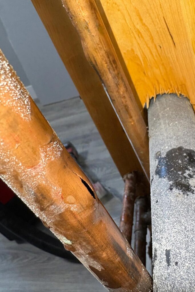 Close-up of a burst copper pipe split open from freezing in a Calgary home.
